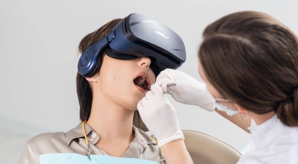 Le dentiste travaille sur le traitement des caries, tandis que son patient porte les lunettes VR, réalité virtuelle dentisterie pédiatrique