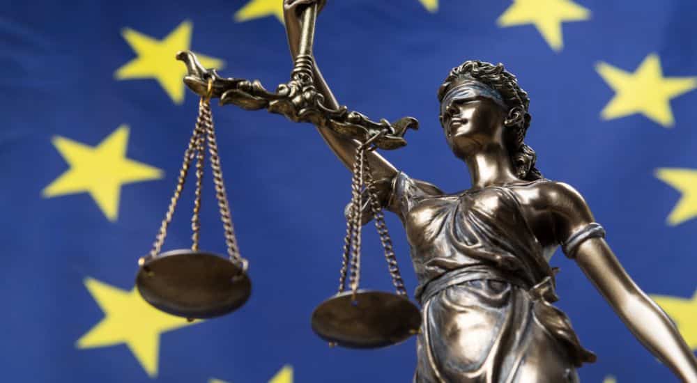 Statue de la déesse les yeux bandée de la justice, contre un drapeau européen, condamnation de Mut’Est