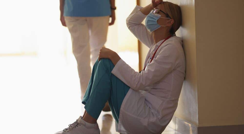 Soignante assise sur le sol, la main sur le front, violences en santé