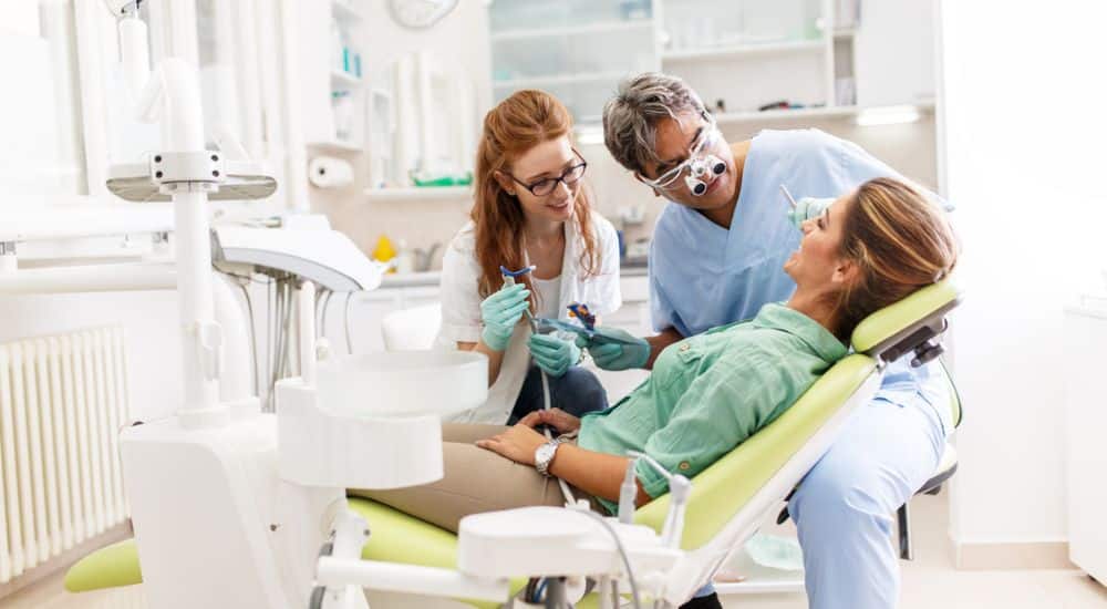 Chirurgien-dentiste accompagné d'une étudiante stagiaire, devant un patient. Maître de stage actif