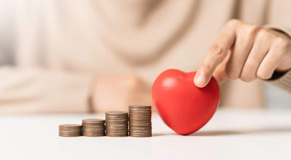 Femme tenant en forme de cœur rouge et pile de pièces d’argent. Dépenses de soins dentaires en 2024