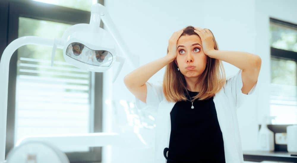 Jeune femme chirurgien-dentiste, les mains posées sur la tête, mimant un stress ou une exaspération. Proposition de PLFSS 2026