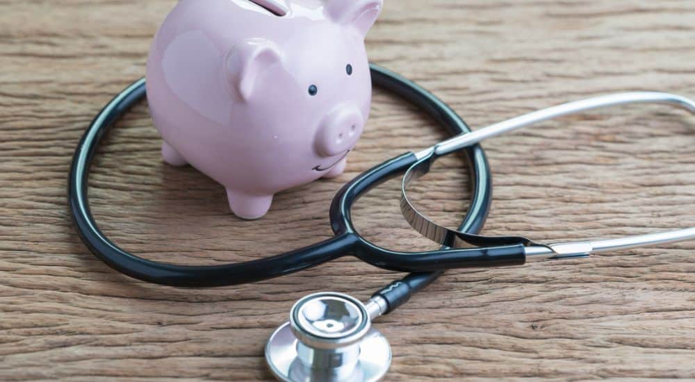 Stéthoscope avec une tirelire rose sur une table en bois, augmentation des dépenses de santé