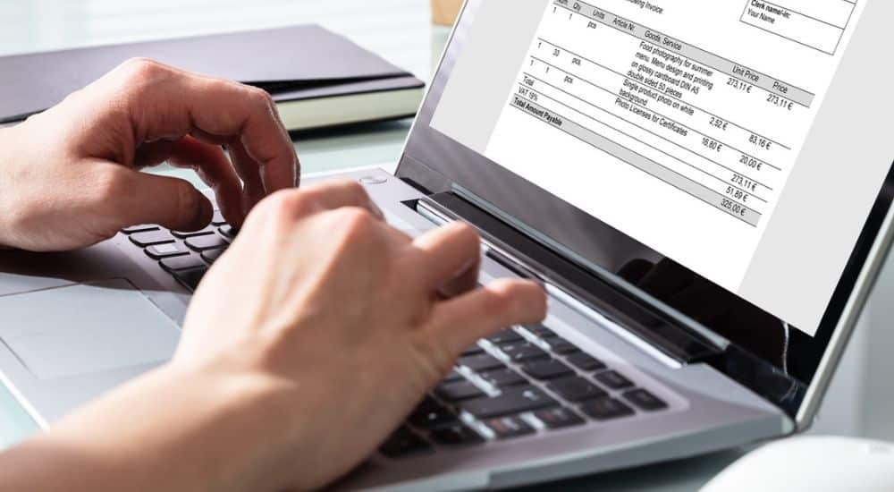 Mains en gros plan, éditant une facture sur un ordinateur portable. Facturation électronique